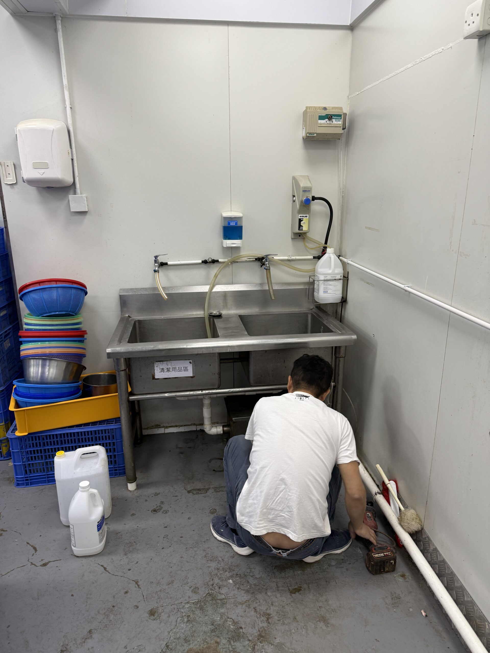 技工於不鏽鋼水槽下進行喉管接駁工程，施工嚴謹確保滴水不漏